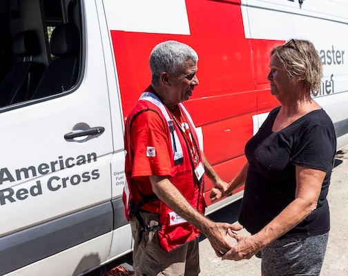 The Renewed Hope Foundation volunteer holding hands with woman in front of The Renewed Hope Foundation vehicle.